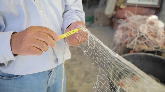 Pescatore sta cucendo la sua rete prima di andare in barca a mare di mattina.