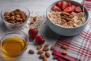 Healthy vegan breakfast bowl: oatmeal with banana, strawberry, honey and nuts on white background.