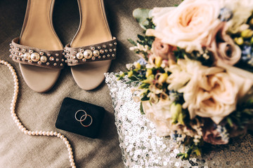 Wedding accessories on a pillow with sequins: two silver wedding rings, bridal bouquet, shoes and beads with pearls. Romantic greeting card, engagement, celebration, invitation, love. Photos in