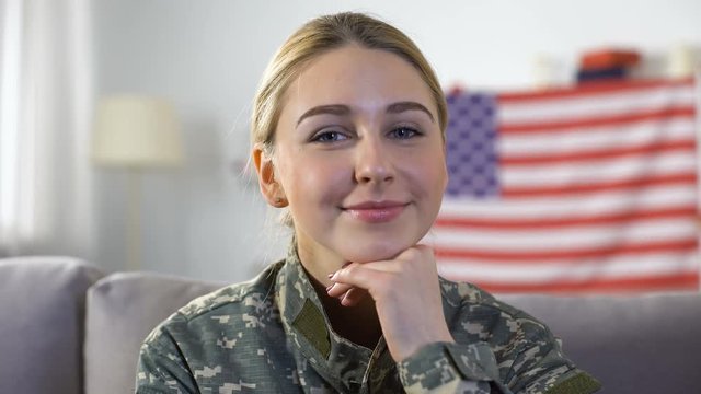 Happy female soldier in uniform smiling into camera, USA flag on background