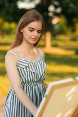 Portrait of Blond hair girl in dress drawing a picture in the park