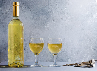 White wine in glass wine glasses, a bottle of wine, corkscrew. Blue background. Copy space