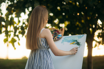 Back view of Blond hair girl in dress drawing a picture in the park