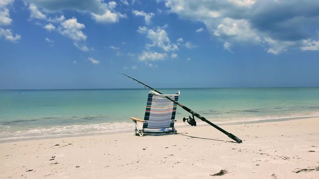 A relaxing lazy beach side afternoon with a view of a folding beach chair and a fishing pole. Waves crushing and then a ship shows in the distance. Clearwater Beach, Florida 2019