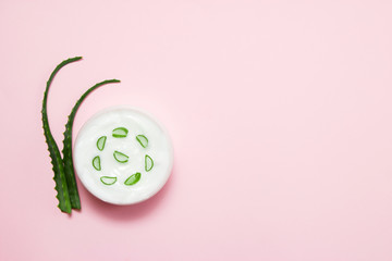 Jar of cream and slice of aloe vera on a pink background. Top view