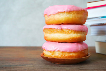 Stack of three strawberry cream donuts on wood table and books stack background.