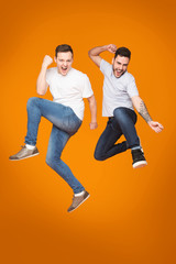 Fototapeta na wymiar Two Friends Jumping And Celebrating Success Over Yellow Background