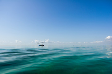 Tropical sea quiet blue sky with clouds and transparent water that allow to see the seaweed background. Fisherman's boat on the horizon.