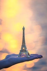 Hand holding a figurine of Eiffel tower during sunset . french culture .