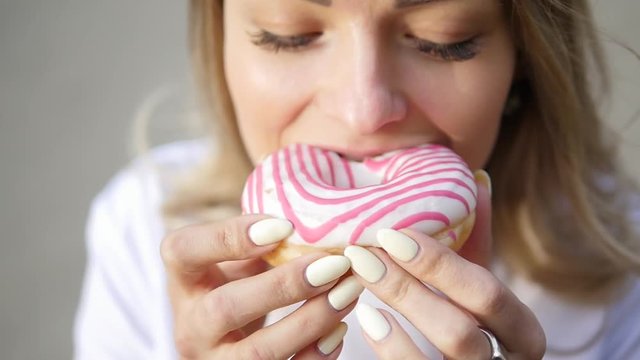 Close up of a woman who is eating donut with colorful frosting and smiling.