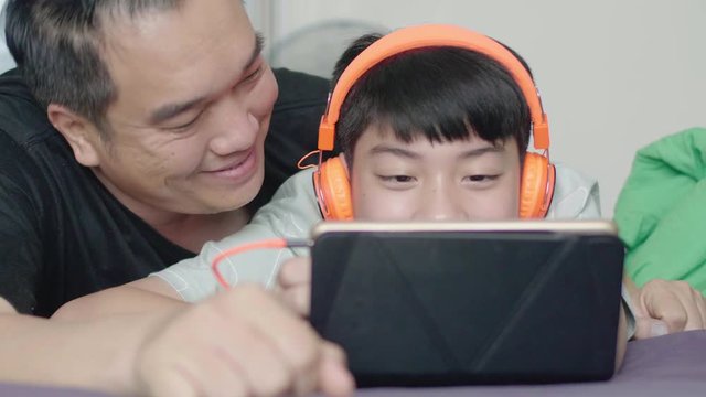 Father and son enjoying a movie on tablet computer with smiling face at home