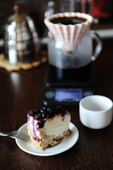 Piece of blueberry cheesecake on a white plate side view. Coffee in origami dripper. Delicious dessert
