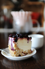 Piece of blueberry cheesecake on a white plate side view. Coffee in origami dripper. Delicious dessert