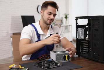 Male technician repairing power supply unit at table indoors