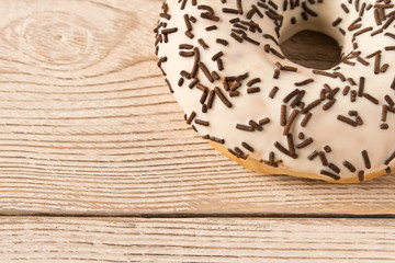 Fresh glazed donut with chocolate sprinkles on a wooden table.