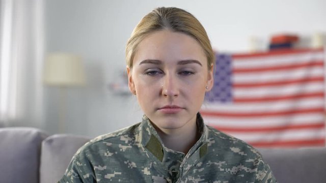 Crying american female soldier looking at camera against US national flag, PTSD