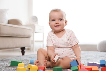 Cute baby girl playing with building blocks in room