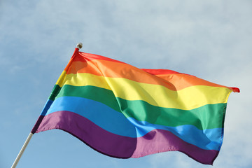 Bright rainbow gay flag fluttering against blue sky. LGBT community