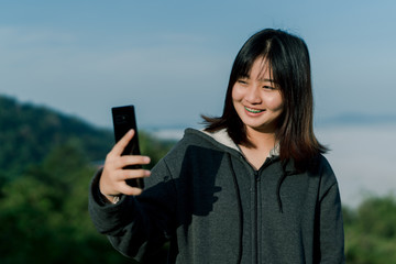 Asian woman Wearing a winter jacket, take a selfie phone, take pictures in the tourist area behind the fog and mountains with a smiling face