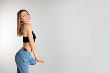 Fototapeta na wymiar Slim woman in oversized jeans on light background, space for text. Perfect body