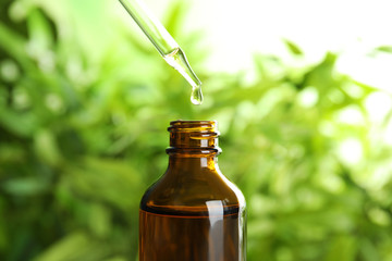 Essential oil dripping from pipette into glass bottle on blurred background, closeup