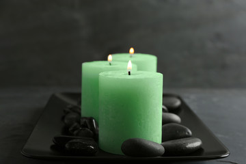 Fototapeta na wymiar Dark plate with three burning candles and rocks on table