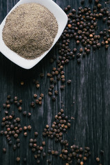 Black peppercorns in white bowl on wooden background