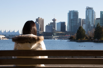 Woman sit on the bench at Stanley Park with Vancouver landmark in background. Stanley Park and seawall in Vancouver, Canada. It is largest urban park with beaches, trails, scenic seawall