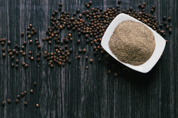 Black peppercorns in white bowl on wooden background
