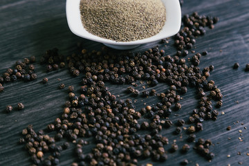 Black peppercorns in white bowl on wooden background
