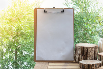 Blank white paper on clipboard copy space for text on wooden table with green tree in a garden as background.