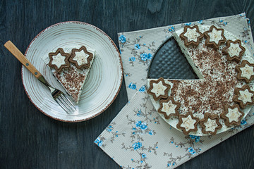 Cottage cheese cake (without baked cheesecake) is decorated with cookies and grated black chocolate on a dark wooden background.