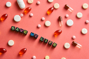 Multicolored title SAVE MY LIFE from black cubes on the table with tablets on coral background