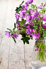 Wild violet flowers in glass bottle on rustic wooden table background.