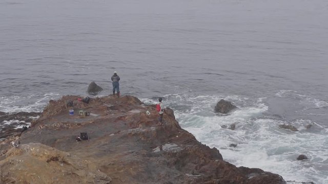 long shot of fishermen fishing on the rocky edge of the foggy ocean
