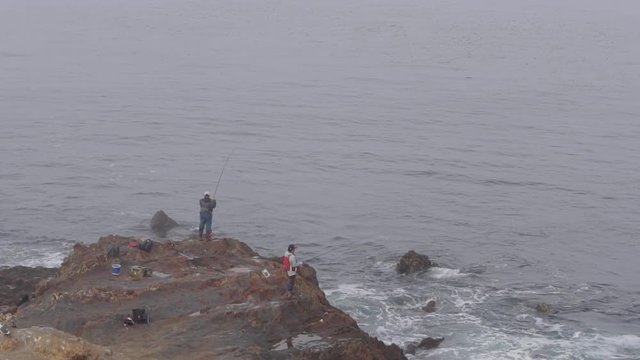 long shot of fishermen fishing on the rocky edge of the misty ocean