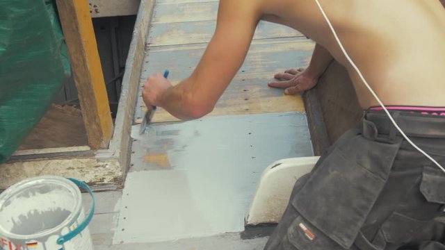 Painting deck planking of wooden boat with protective exterior paint.