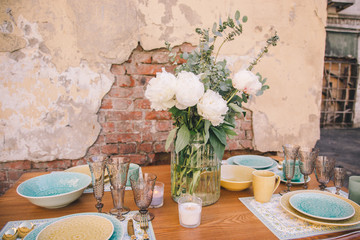 The decor and table setting for a meal or a holiday. Tablewares on a table against a brick wall. A bouquet of white flowers. Dishes in oriental style