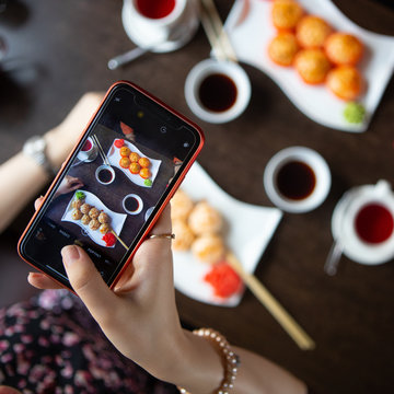 A girl using the phone takes pictures of rolls and sushi in a restaurant