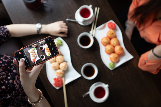 A girl using the phone takes pictures of rolls and sushi in a restaurant