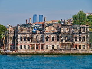 Bosporus strait, view from cruise ship. Old traditional damaged wooden building with structural support and TAT twin towers at the background.