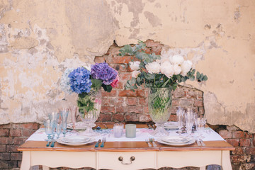 The decor and table setting for a meal or a holiday. Tablewares on a table against a brick wall. A bouquet of colorful flowers. Tableware and decor