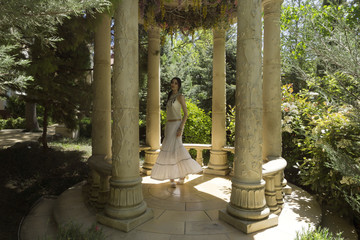 A young woman in a long white skirt whirls in dance in the gazebo of old park