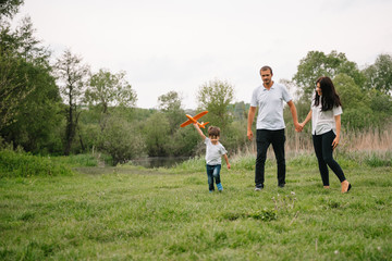 Fototapeta premium Father, mother and son playing with toy airplane in the park. friendly family. People having fun outdoors. Picture made on the background of the park and blue sky. concept of a happy family.
