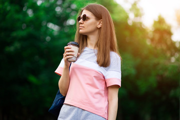 Pretty student girl in sunglasses drinking coffee at summer park