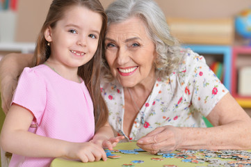 Cute little granddaughter and grandmother collecting puzzles