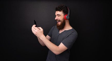 Photo of a happy man with beard, lisntening music and using phone over isolated background