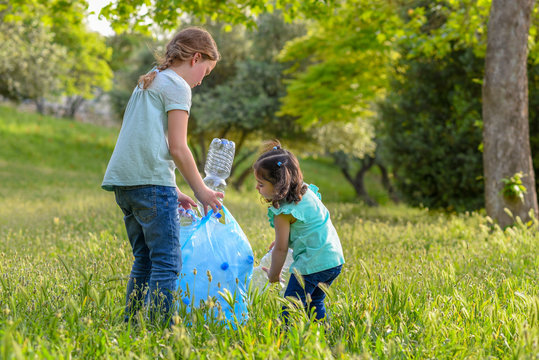 Little Girls Takings Plastic Bottles From Grass. Children Picking Up Litter In The Park .