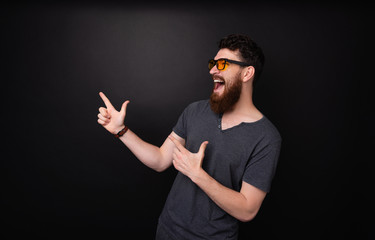 Excited bearded guy poiting away with fingers and screaming over dark background