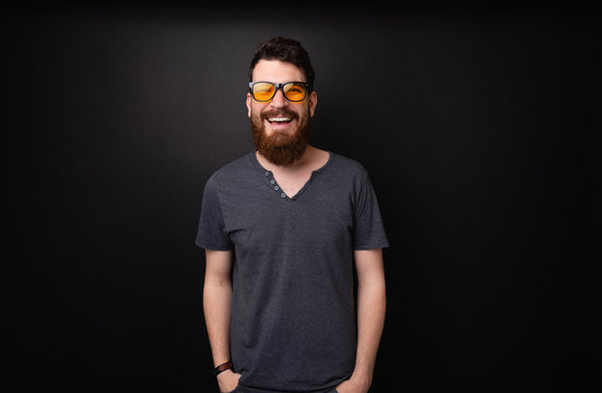 Photo of bearded guy wearing stylish sunglasses, smiling at camera over dark background